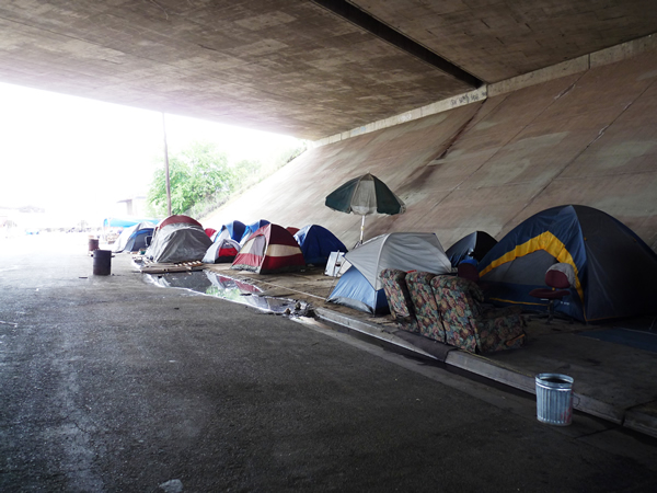 A Homeless Encampment situated in Fresno, California, USA. Encampments under highway overpasses are common in the US, not only for the structural protection from the elements, but because highway property is not part of city jurisdictions and can avoid the frequent evictions of police faced by those on other public property. Photo by Christopher Herring.