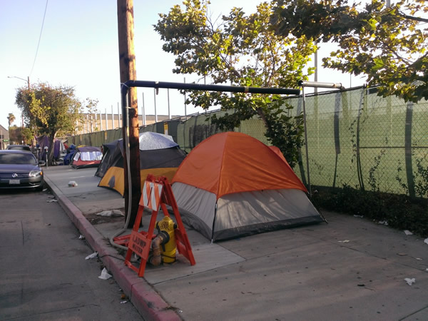 Tents:  A temporary homeless encampment on the sidewalk bordering the campus of the Los Angeles City College in Los Angeles, U.S.A.  The City College is a community institution that provides a stepping stone to full-degree programs at other colleges and universities.  Inside the fence, 20,000 mainly low- and lower-income students pursue their dreams of a better life .  Outside the fence, the main preoccupation is to find a place to sleep.  Photograph by Benjamin Clavan, 2015.